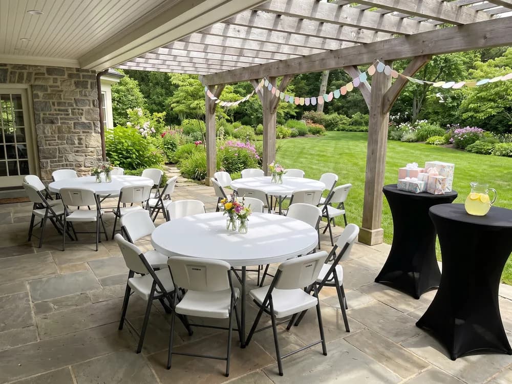 Round tables and white folding chairs on a covered flagstone patio, gifts on two cocktail tables at the edge